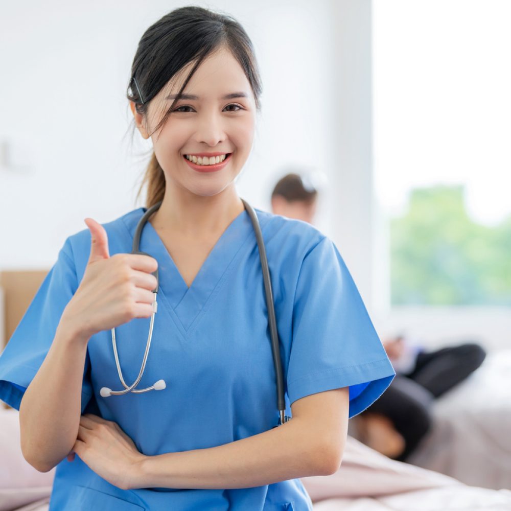 Young Asia pretty doctor sitting at nursing home with smile and thumb up. Put a stethoscope around neck. Medical health care worker in blue uniform work at clinic or hospital. Business healthcare