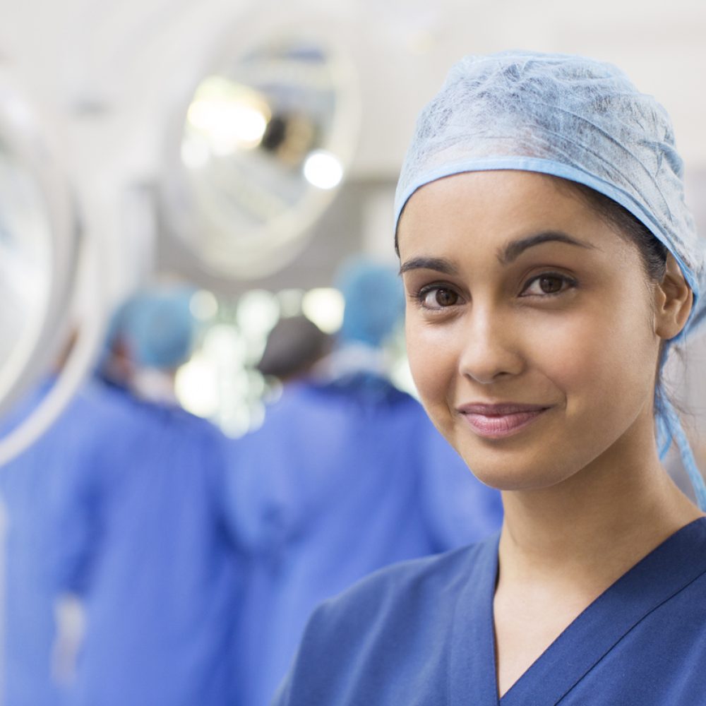 Portrait of smiling female surgical nurse wearing blue surgical cap and scrubs